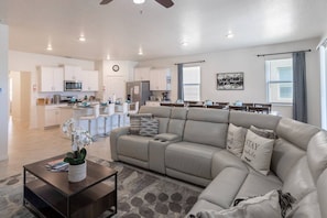 Plush living room with 75in smart OLED TV + dining area with seats for 12 at table and 4 at countertop.