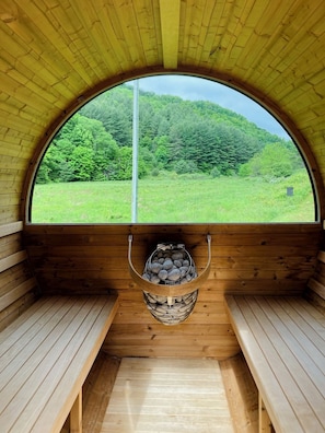 Cedar barrel sauna with a view of the meadow and mountainside.