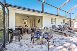 Screened in pool area w/chasers, umbrella, table, and lanai with sofas.
