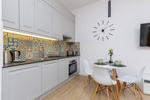 A modern kitchen with white cabinetry, a dining area, and decorative tiles.
