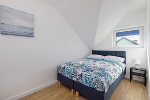 A comfortable bedroom featuring a large bed with soft blue bedding. A window allows plenty of natural light to fill the space.