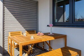A small balcony with a wooden table and chairs, perfect for enjoying a morning coffee outdoors. The setup overlooks a serene landscape.