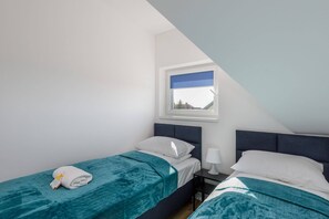 A neatly arranged twin bedroom with two single beds dressed in turquoise bedding. A large window provides a peaceful view outside.