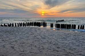 A breathtaking sunset over the sea, with the vibrant orange and yellow hues of the sun reflecting on the water. Wooden posts rise from the waves, adding to the scenic beauty.
