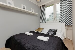 A comfortable bedroom featuring a double bed with grey bedding and white towels neatly placed. The room is bright and minimalistic, perfect for relaxation.