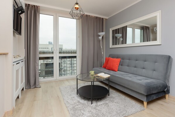 A cozy living room with a grey sofa, a small round coffee table, and floor-to-ceiling windows. The natural light enhances the modern and inviting design.