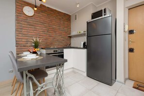 A compact and functional kitchen with a dining area for two. It features a sleek refrigerator and stylish decor in neutral tones.