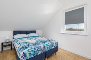A comfortable bedroom featuring a large bed with soft blue bedding. A window allows plenty of natural light to fill the space.