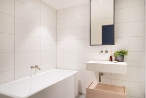 A pristine bathroom has white tiled walls, a vanity, full-sized bathtub, and a shower; and is stocked to get you started with towels and consumables