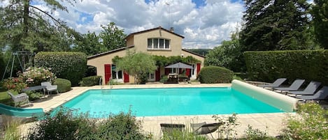 La maison avec la grande piscine, son volet securisé et ses transats.