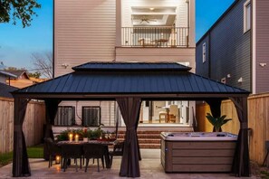 The outdoor space features a pergola, hot tub, and dining table