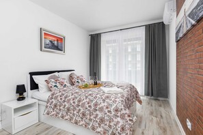 Cozy bedroom with a comfortable double bed, stylish bedding, and access to natural light through large windows.
