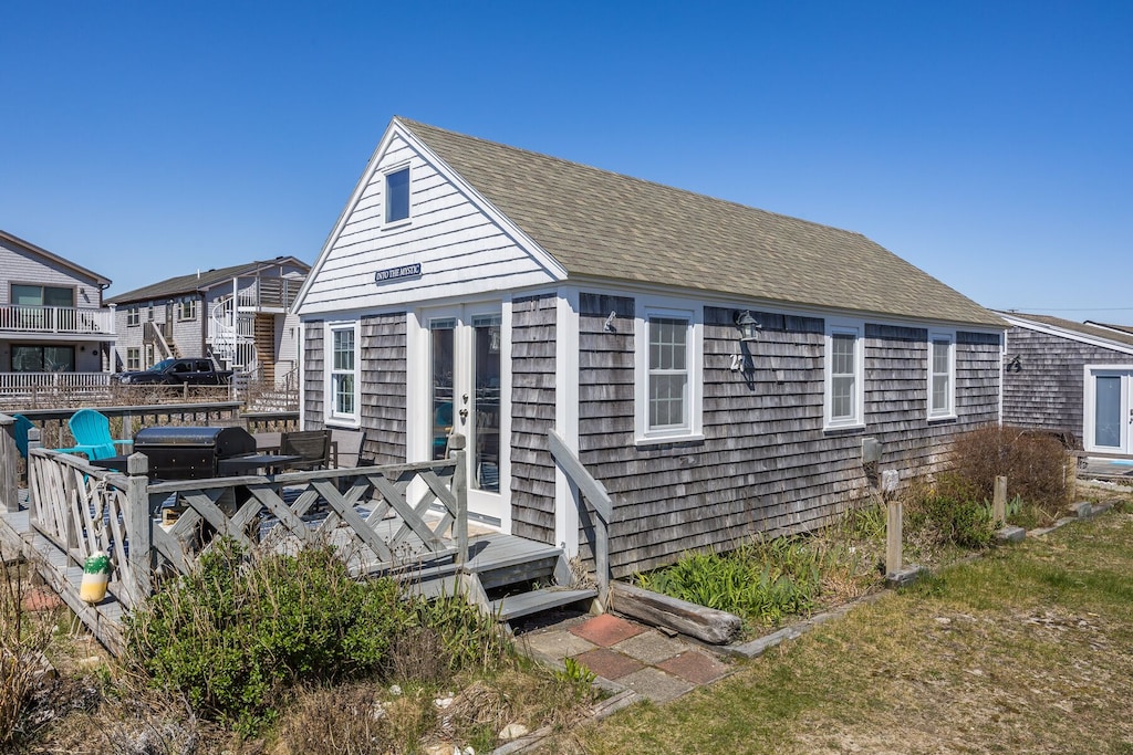 A classic gray cottage in Provincetown is nestled between other vacation rental cottages with green grass and shrubbery surrounding and a deep blue sky overhead.