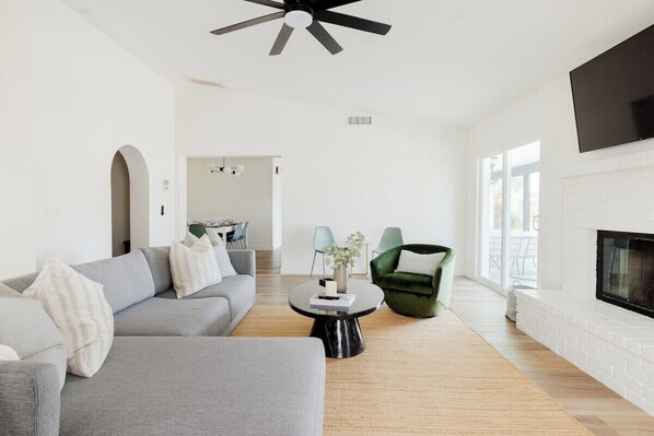 Main living room area with vaulted ceilings, fireplace, TV w/ Netflix, large sofa, game room and laundry. Walk-out patio sliding door to backyard covered seating area and pool.