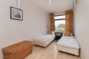 A simple bedroom featuring two single beds, a small bedside table, and a woven basket for storage.