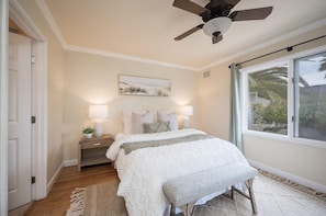 Indulge in the ultimate relaxation in this spacious vacation rental bedroom, featuring a comfortable queen size bed, plenty of natural light from the many windows, a soothing ceiling fan, and a private ensuite bathroom for your convenience.