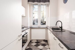 A modern kitchen with white cabinets, a black countertop, and a black-and-white checkerboard-patterned floor.