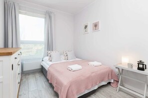 A comfortable bedroom featuring a queen-size bed with pink bedding, a bedside table, and a large window covered with light curtains.