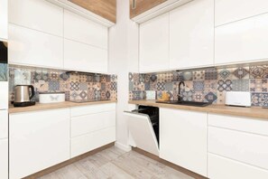 A modern white kitchen with sleek cabinets and patterned backsplash tiles. The space is clean and bright.