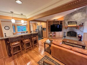 Living area with wood burning fireplace, TV, desk and breakfast bar to kitchen