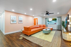 The main living area features a stunning orange leather sectional, a 70-inch 4K HDTV with cable, a premium sound system, stylish retro décor, and an abundance of natural light.