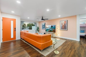 The main living area features a stunning orange leather sectional, a 70-inch 4K HDTV with cable, a premium sound system, stylish retro décor, and an abundance of natural light.