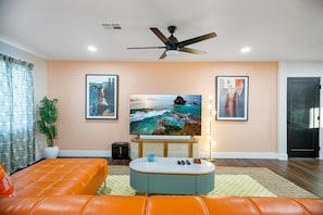 The main living area features a stunning orange leather sectional, a 70-inch 4K HDTV with cable, a premium sound system, stylish retro décor, and an abundance of natural light.