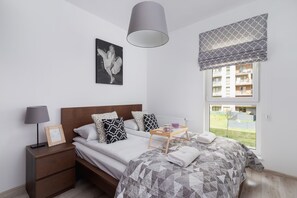 A stylish bedroom with a comfortable double bed, gray bedding, and a matching nightstand. A modern table lamp and a decorative framed artwork add to the cozy and elegant atmosphere.