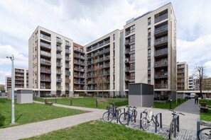 An exterior shot of a modern apartment complex with multiple balconies and a green courtyard. The building features a contemporary architectural design.