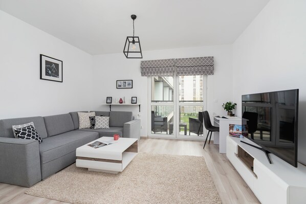 A modern living room featuring a gray sectional sofa, a white coffee table, and a TV mounted on a sleek entertainment unit. The decor is minimalistic with a black-and-white color scheme.