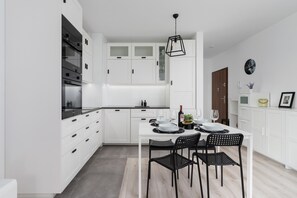 A modern kitchen with white cabinetry, a black dining table, and pendant lighting. The open layout seamlessly connects with the living area.