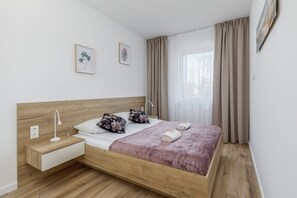 A modern bedroom with a wooden bed frame, nightstand, and soft pastel bedding.