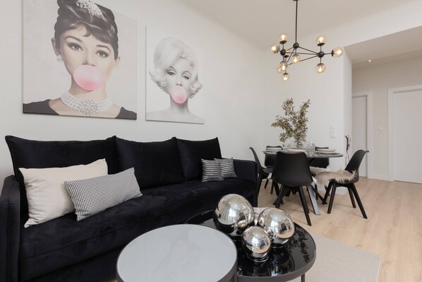 A stylish and modern living room with a black sofa, decorative pillows, and artistic wall decor featuring portraits, creating an elegant ambiance.