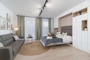 A full view of the studio, combining the sofa area, dining table, and sleeping arrangement in a seamless layout.

