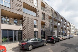 A view of the apartment building’s facade, showcasing modern architecture and on-street parking.