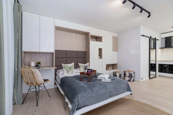 A full view of the studio, combining the sofa area, dining table, and sleeping arrangement in a seamless layout.