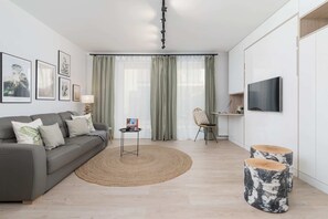 A cozy open-plan space featuring a gray sofa, a round woven rug, and a small dining table with chairs.