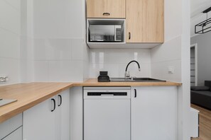 A compact kitchen with white cabinets, a wooden countertop, and modern appliances for convenient cooking.