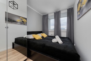 A cozy bedroom featuring a double bed, black bedding, and yellow accent pillows, creating a fresh and inviting ambiance.