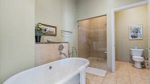 A bathroom with a standalone bathtub, a walk-in shower, and a toilet. A towel hangs on the tub, and a picture and decorative items are displayed on the wall shelf above the tub.