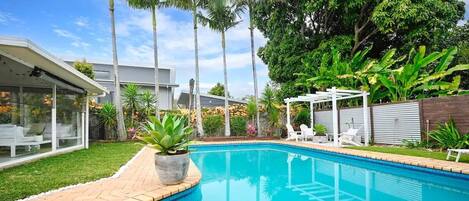 Large glistening pool. House sun room with drop down cafe blinds shown on the left of the photo