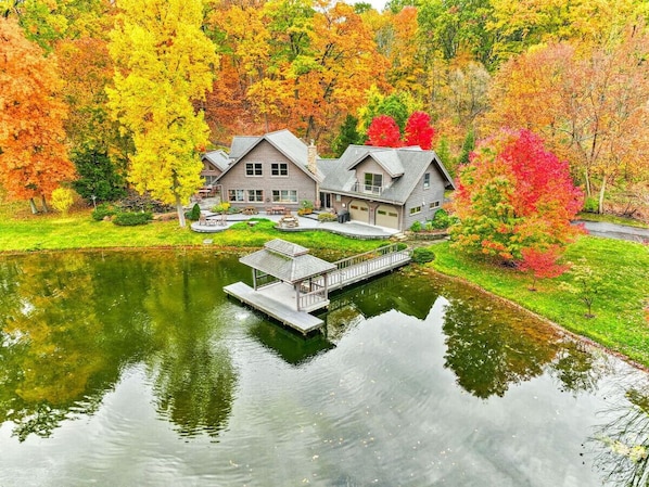 Back of house with pass-through garage doors, large deck with grill, patio with Solo Stove fire pit, and main dock on the koi pond