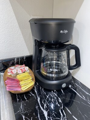 Coffee maker with coffee, sugar, creamer and coffee filters. Two to go coffee cups with lids.