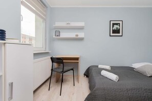 Another view of the bedroom, showing a work desk and a window letting in natural light.
