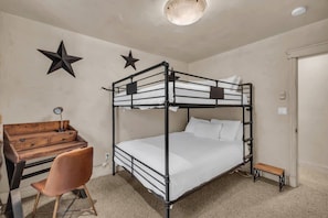 The stylish bunk room features a queen-over-queen bunk bed, a bean bag chair, a mounted 32” TV,  two large closets, and a workspace with a desk and chair.