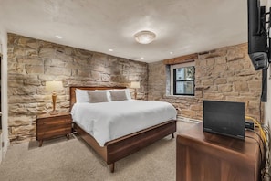 The cozy master bedroom room features a king-size bed with matching side tables, a dresser with a 50” mounted TV above, a spacious walk-in closet, and an attached bathroom.