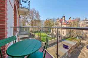 A charming balcony with green chairs, a table, and a view of historic buildings.