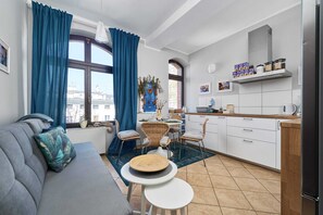 A modern living room space with a small round dining table, a gray couch, and a large window.