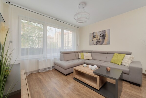 A bright and cozy living area with a gray sofa, yellow cushions, and natural light pouring in through large windows.