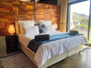 King bed with 100% cotton linen in the primary bedroom. Please note that wooden wall does not go all the way to the floor or ceiling allowing aircon air in summer and fireplace heat. in winter to circulate freely. 